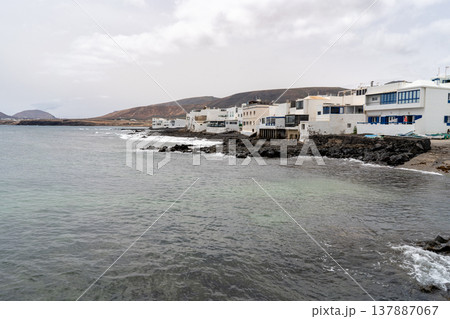 A coastal view of Punta Mujeres in Lanzarote, featuring white buildings and serene ocean water under a cloudy sky. 137887067
