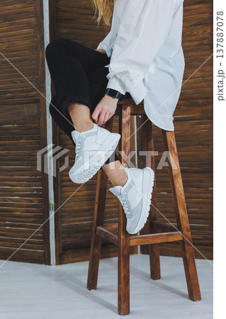 Close-up of female legs in black jeans in stylish leather white sneakers. Fashionable woman in new sneakers. Modern seasonal collection of stylish sneakers. Women's fashion. Close-up of female legs in black jeans in stylish leather white sneakers. Fashionable woman in new sneakers. Modern seasonal collection of stylish sneakers. Women's fashion. 137887078