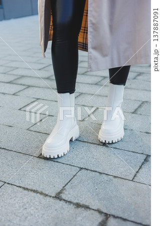 A cute young woman in a beige raincoat and autumn leather boots walks down the street. Autumn warm image. Women's fashion A cute young woman in a beige raincoat and autumn leather boots walks down the street. Autumn warm image. Women's fashion 137887091