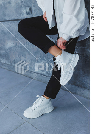 Women's legs in black trousers and white leather sneakers. Modern casual style. New shoe collection 137887143
