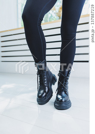 Female legs in black leather boots close-up. Autumn women's boots without a heel Female legs in black leather boots close-up. Autumn women's boots without a heel 137887219