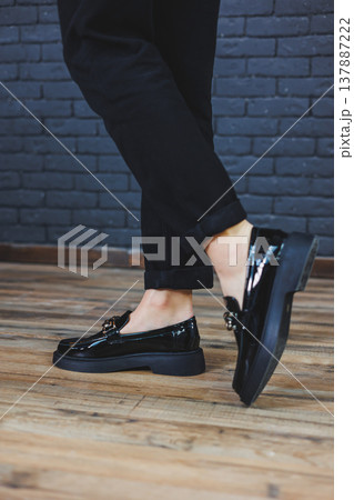 Close-up female legs in black trousers and leather black shoes. Women's shoes in patent leather with a metal buckle. New spring-summer collection of women's leather shoes 2022 Close-up female legs in black trousers and leather black shoes. Women's shoes in patent leather with a metal buckle. New spring-summer collection of women's leather shoes 2022 137887222
