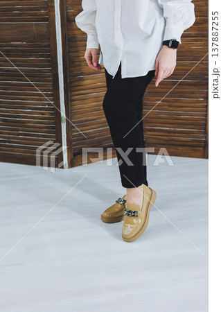 Close-up of female legs in black jeans in stylish leather beige shoes. Fashionable woman in new loafers. Modern seasonal collection of stylish shoes. Women's fashion. 137887255