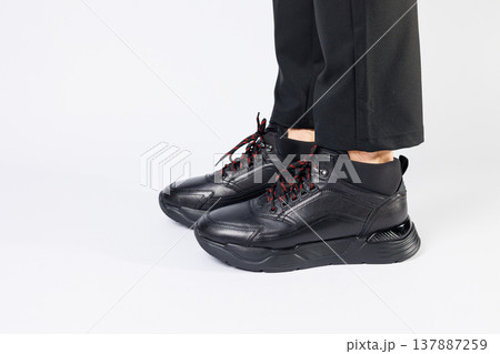 Stylish leather black short men's autumn sneakers on a white background on men's legs. Sneakers winter collection 2022. Stylish leather black short men's autumn sneakers on a white background on men's legs. Sneakers winter collection 2022. 137887259