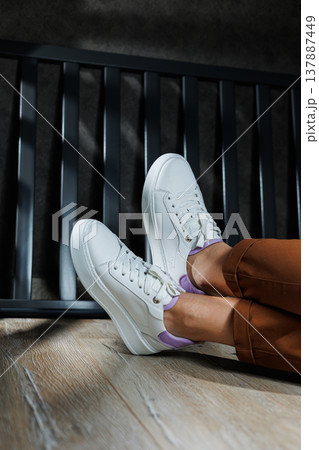 White leather sneakers on women's legs. Women's legs in comfortable casual sneakers 137887449