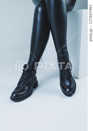 Female legs in leather black autumn boots. A fashion girl stands in a store and measures shoes. 137887462