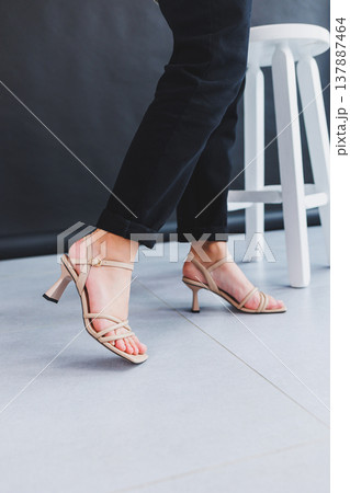 Women's legs close-up in summer brown flip-flops with heels. Summer collection of shoes for women made of genuine leather Women's legs close-up in summer brown flip-flops with heels. Summer collection of shoes for women made of genuine leather 137887464