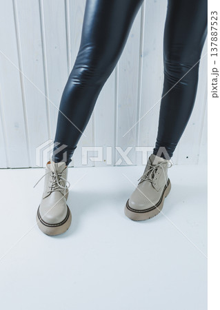 Female legs in leather beige autumn boots. A girl stands in a store and measures shoes. Female legs in leather beige autumn boots. A girl stands in a store and measures shoes. 137887523