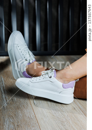 White leather sneakers on women's legs. Women's legs in comfortable casual sneakers 137887643