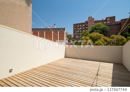 A modern terrace with wooden flooring and a clear blue sky. Surrounding buildings and greenery are visible in the background. 137887749