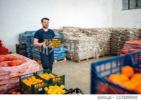 Man smiling carrying a crate of fresh produce in warehouse Man smiling carrying a crate of fresh produce in warehouse 137889008