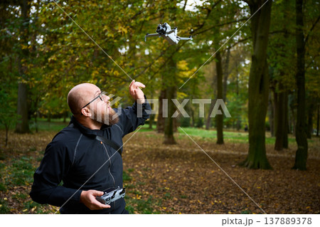 Man playing with drone in autumn park, flying quadcopter with remote controller, outdoor hobby and leisure activity, modern technology and recreation concept Man playing with drone in autumn park, flying quadcopter with remote controller, outdoor hobby and leisure activity, modern technology and recreation concept 137889378