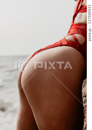 Swimsuit buttocks skin female model wearing red strappy swimwear while posing by the ocean coastline on a sunny summer day 137890931