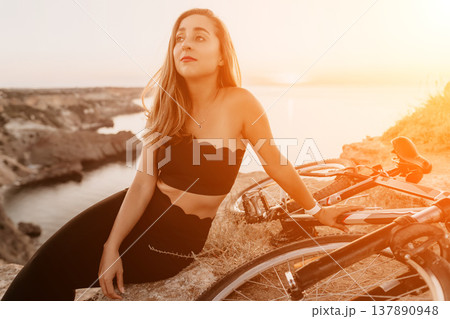 Woman bicycle sunset relaxing on a rocky cliff edge by the sea during a golden hour cycling break 137890948