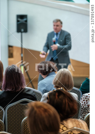 Business speaker giving presentation to audience at professional conference, attendees listening in seats 137891493