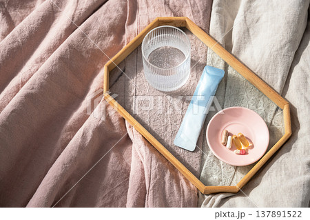 Dietary supplements and water in glass on wooden tray placed on bed. Dietary supplements and water in glass on wooden tray placed on bed. 137891522