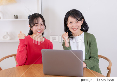 パソコンを操作しながらガッツポーズをする母と娘 137891556