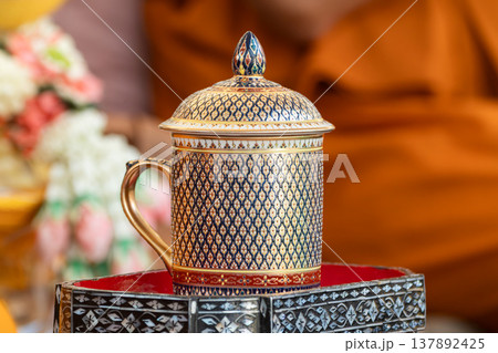 Thai ceramic cup with detailed gold and blue pattern placed on a decorative tray with a warm indoor background highlighting handcrafted design. 137892425