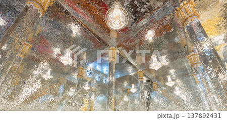 Mirror mosaic ceiling inside a temple with multiple light fixtures creating a reflective surface that forms bright patterns and detailed architectural design. 137892431