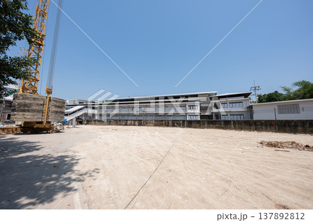 Empty construction site with cleared ground and building structure in background. Wide open land prepared for development and construction work. Empty construction site with cleared ground and building structure in background. Wide open land prepared for development and construction work. 137892812