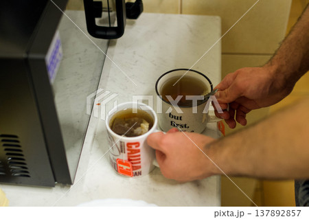 A man pours tea into two mugs on the kitchen table. The concept of comfort, hospitality, and everyday life, morning rituals, warmth, relaxation, and a homey lifestyle. A man pours tea into two mugs on the kitchen table. The concept of comfort, hospitality, and everyday life, morning rituals, warmth, relaxation, and a homey lifestyle. 137892857