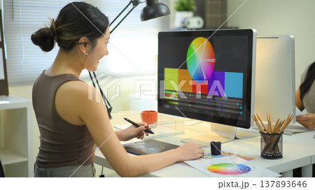 Graphic designer woman working on creative desk computer while using graphic tablet at desk in the office Graphic designer woman working on creative desk computer while using graphic tablet at desk in the office 137893646