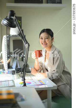 Smiling businesswoman holding coffee mug at office desk, relaxed professional work moment 137893676