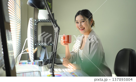 Smiling businesswoman holding coffee mug at office desk, relaxed professional work moment Smiling businesswoman holding coffee mug at office desk, relaxed professional work moment 137893804