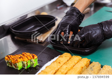 Sushi Rolls Being Packed Into Container By Chef Wearing Black Gloves, Vibrant Avocado And Tempura 137894599