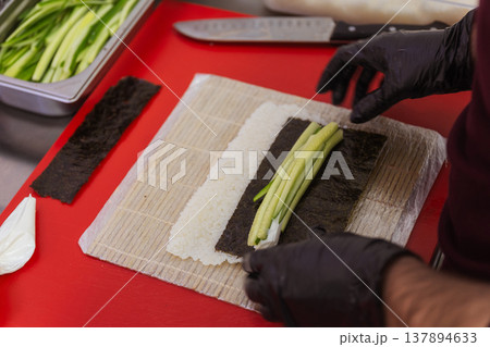 Chef Rolling Cucumber Rice On Mat With Black Gloves, Bamboo Mat Pressed To Shape Tight Roll, Thin Chef Rolling Cucumber Rice On Mat With Black Gloves, Bamboo Mat Pressed To Shape Tight Roll, Thin 137894633