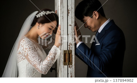 Wedding - Asian Bride and Groom Separated by Rustic White Door Touching Hands in Emotional Moment 137894902