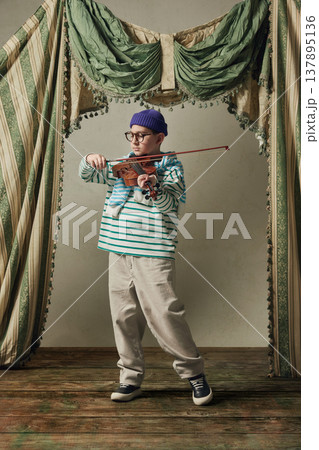 Young boy playing violin in studio with vintage curtains expressive performance. 137895136