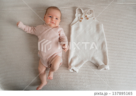 Top view of newborn baby next to baby clothes. Concept of preparation, shopping and early parenting essentials. Top view of newborn baby next to baby clothes. Concept of preparation, shopping and early parenting essentials. 137895165