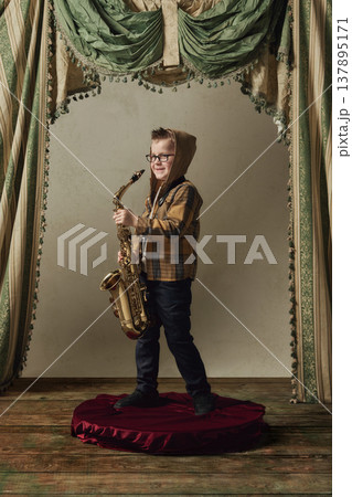 Little boy holding saxophone smiling after performance on stage. Little boy holding saxophone smiling after performance on stage. 137895171