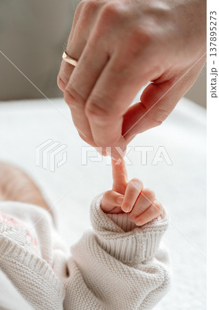 Close-up of newborn baby grasping mother finger. Emotional detail of early bonding and maternal care. Concept of motherhood, protection and gentle parenting. 137895273
