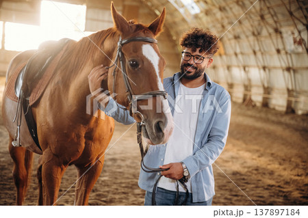Positive facial expression, smiling. Man is with horse in the hangar 137897184