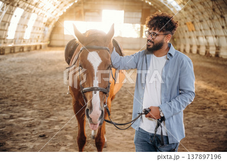 In glasses, standing. Man is with horse in the hangar In glasses, standing. Man is with horse in the hangar 137897196