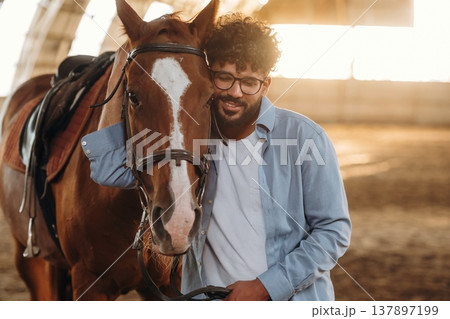 Front view, standing together. Man is with horse in the hangar Front view, standing together. Man is with horse in the hangar 137897199