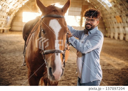 Secures the saddle. Man is with horse in the hangar Secures the saddle. Man is with horse in the hangar 137897204
