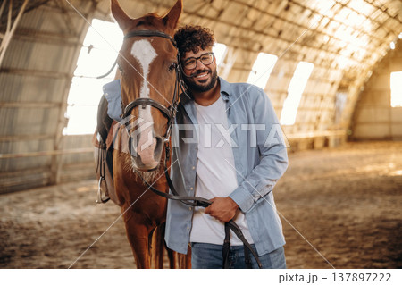 Front view, standing together. Man is with horse in the hangar Front view, standing together. Man is with horse in the hangar 137897222