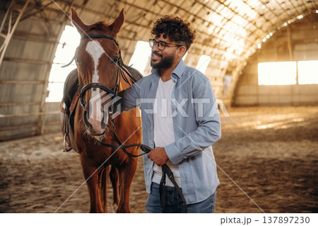 In casual clothes, standing by. Man is with horse in the hangar 137897230