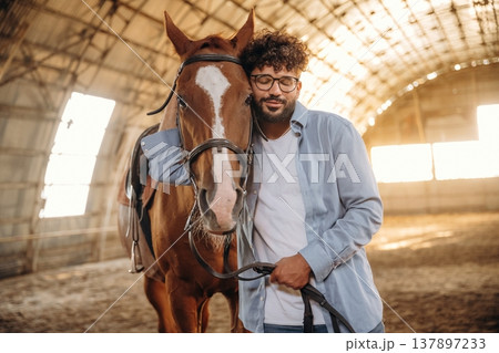 In casual clothes, standing by. Man is with horse in the hangar In casual clothes, standing by. Man is with horse in the hangar 137897233