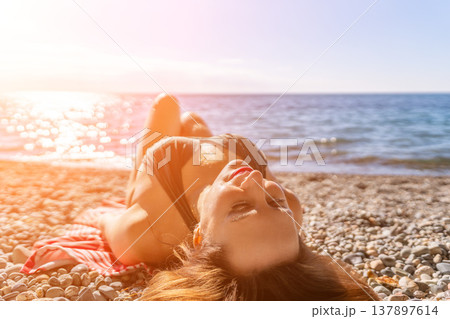 Woman sunbathing beach young woman in bikini lies on pebble shore enjoying golden hour sun and ocean view 137897614