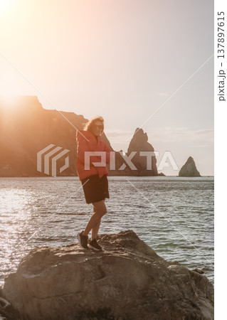 Woman sunset travel scenery shows a young female adventurer in a pink jacket standing on a rock by the coastal cliffs 137897615