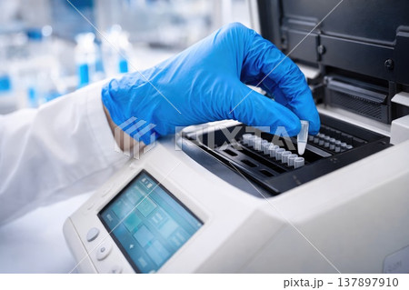 Scientist placing sample into laboratory analyzer with blue gloves close up 137897910