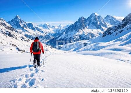Hiker Walking Through Snowy Alpine Mountains Landscape with Backpack and Trekking Poles 137898130