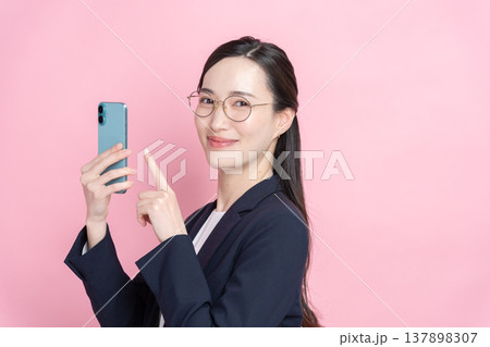 スマホを使う笑顔のビジネスウーマン(ピンクバック・春) スマホを使う笑顔のビジネスウーマン(ピンクバック・春) 137898307