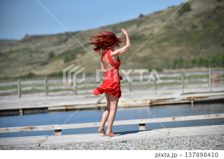 Back view of woman with red hair in red dress by pool 137898410