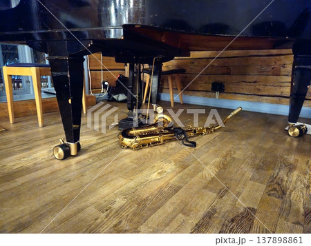 A tenor saxophone rests on the stage floor beneath a grand piano. A tenor saxophone rests on the stage floor beneath a grand piano. 137898861