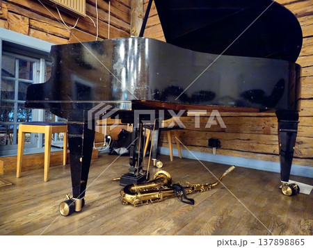 A tenor saxophone rests on the stage floor beneath a grand piano. A tenor saxophone rests on the stage floor beneath a grand piano. 137898865